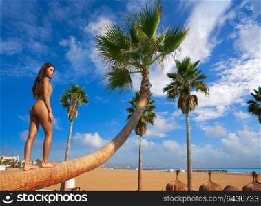 Beautiful woman standing on bent palm tree trunk at the beach