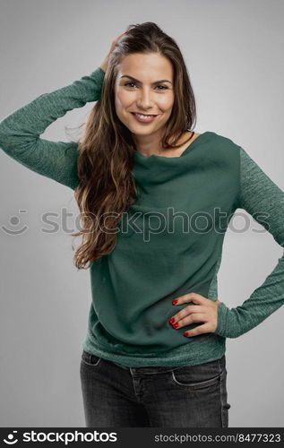 Beautiful woman standing over a gray background with her hand on the hair and smiling