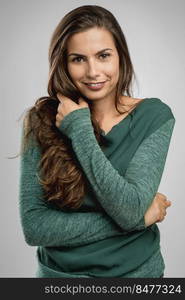 Beautiful woman standing over a gray background with her hand on the hair and smiling