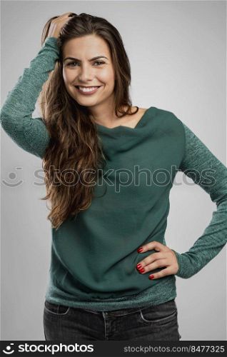 Beautiful woman standing over a gray background with her hand on the hair and smiling