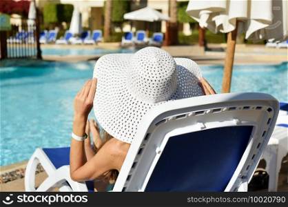 Beautiful woman sunbathing on a beach at tropical travel resort, enjoying summer holidays. Girl holding a hat with her hands on sun lounger near the pool.. Beautiful woman sunbathing on a beach at tropical travel resort, enjoying summer holidays. Girl holding a hat with her hands on sun lounger near the pool