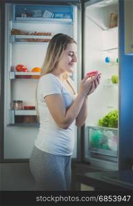 Beautiful woman taking donut from fridge at late evening