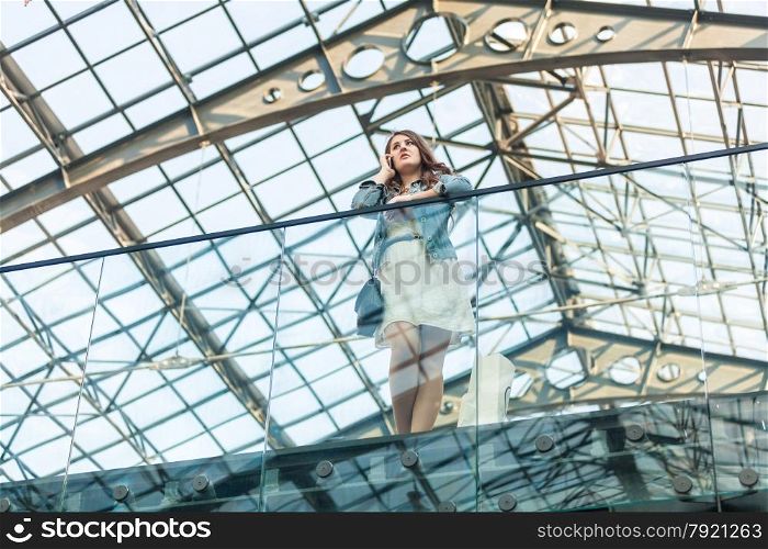 Beautiful woman talking on cellphone at airport with glass ceiling