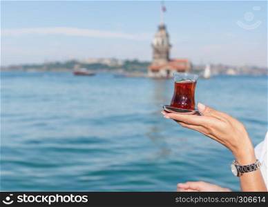 Beautiful woman traveler holds traditional Turkish tea glass in background of Maiden Tower,a popular destination in Istanbul,Turkey