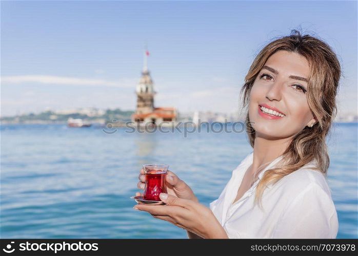 Beautiful woman traveler holds traditional Turkish tea glass in background of Maiden Tower,a popular destination in Istanbul,Turkey. Beautiful woman traveler holds traditional Turkish tea glass in background of Maiden Tower