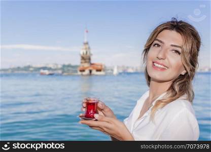 Beautiful woman traveler holds traditional Turkish tea glass in background of Maiden Tower,a popular destination in Istanbul,Turkey. Beautiful woman traveler holds traditional Turkish tea glass in background of Maiden Tower