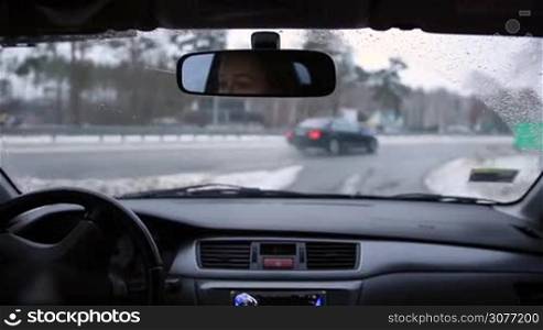 Beautiful woman travelling by car in winter. Female driver&acute;s hands on the steering wheel inside of car while driving and making a turn on the main road in wintertime.