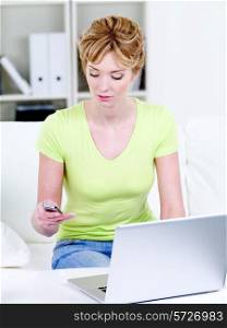Beautiful woman typing sms on mobile phone with laptop at home - indoors