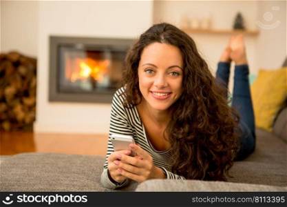 Beautiful woman using a cellphone at home at the warmth of a fireplace
