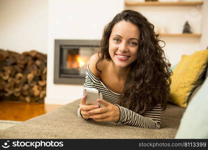 Beautiful woman using a cellphone at home at the warmth of a fireplace