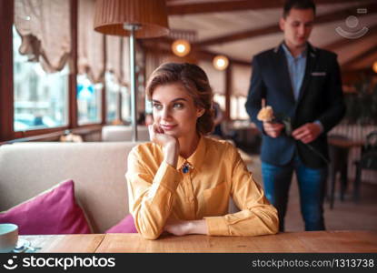 Beautiful woman waiting in restaurant, man with rose in hand on background