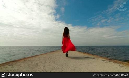 beautiful woman walking down pier in long red dress