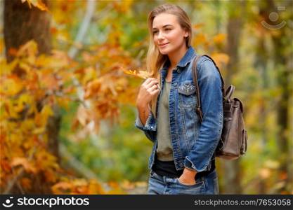 Beautiful woman walking in autumn park with dry tree leaf in hand, enjoying fall weather