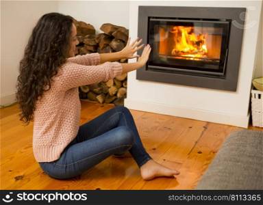 Beautiful woman warming hands on the fireplace