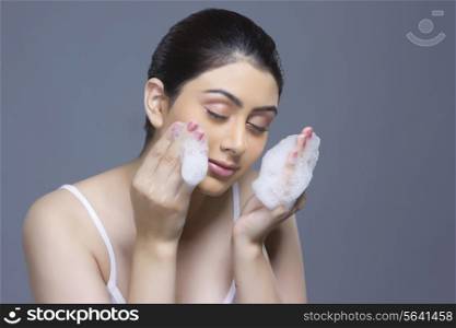 Beautiful woman washing face with soap sud against blue background