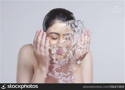 Beautiful woman washing face with water over gray background