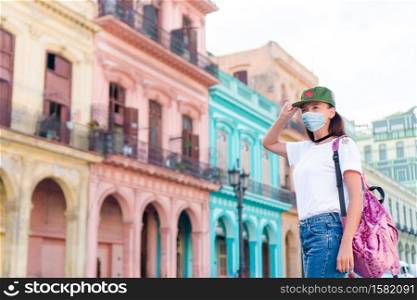 Beautiful woman wearing a mask for prevent virus in popular street in old Havana on Cuba. Tourist girl in popular area in Havana, Cuba. Back view of young woman traveler smiling