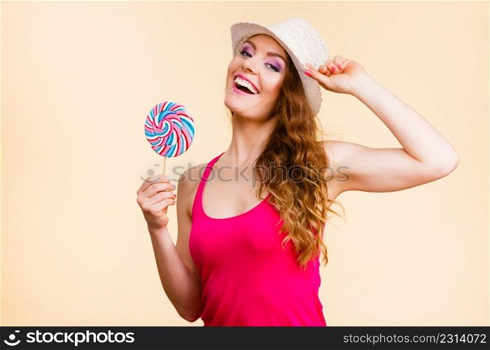 Beautiful woman wearing red tshirt summer hat holding big lollipop candy in hand. Sweet food fun concept. Studio shot on bright beige. Woman holds colorful lollipop candy in hand