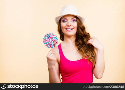 Beautiful woman wearing red tshirt summer hat holding big lollipop candy in hand. Sweet food fun concept. Studio shot on bright beige. Woman holds colorful lollipop candy in hand