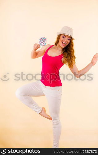 Beautiful woman wearing red tshirt summer hat holding big lollipop candy in hand. Sweet food fun concept. Studio shot on bright beige. Woman holds colorful lollipop candy in hand