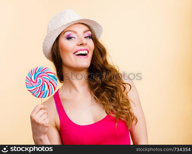 Beautiful woman wearing red tshirt summer hat holding big lollipop candy in hand. Sweet food fun concept. Studio shot on bright beige. Woman holds colorful lollipop candy in hand
