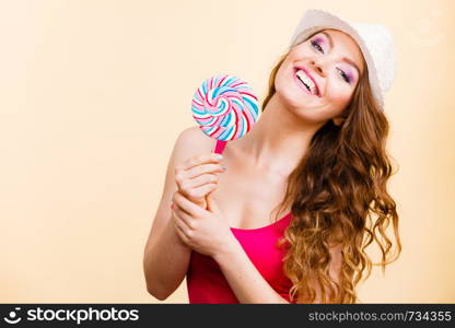 Beautiful woman wearing red tshirt summer hat holding big lollipop candy in hand. Sweet food fun concept. Studio shot on bright beige. Woman holds colorful lollipop candy in hand