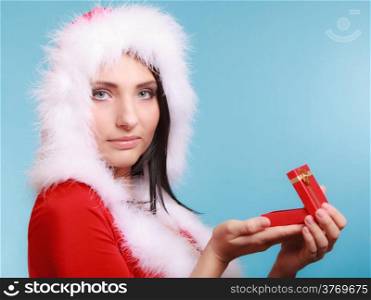 Beautiful woman wearing santa claus costume clothes opening small red gift box with gold bow on blue background. Christmas time gifts.