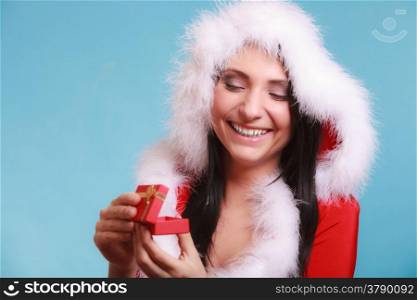 Beautiful woman wearing santa claus costume clothes opening small red gift box with gold bow on blue background. Christmas time gifts.