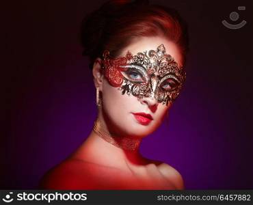 Beautiful Woman Wearing Venetian Masquerade Carnival Mask at Party, over Colorful Background. Christmas and New Year Celebration. Sexy Girl with Holiday Makeup and Red lips. Golden Mask