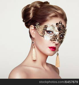 Beautiful Woman Wearing Venetian Masquerade Carnival Mask at Party, over White Background. Christmas and New Year Celebration. Sexy Girl with Holiday Makeup and Red lips. Golden Mask