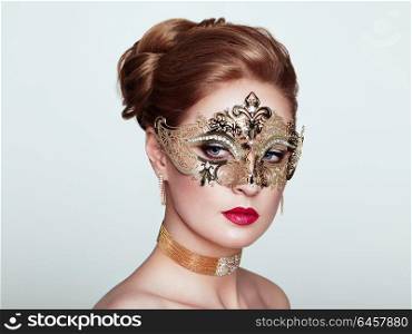 Beautiful Woman Wearing Venetian Masquerade Carnival Mask at Party, over White Background. Christmas and New Year Celebration. Sexy Girl with Holiday Makeup and Red lips. Golden Mask