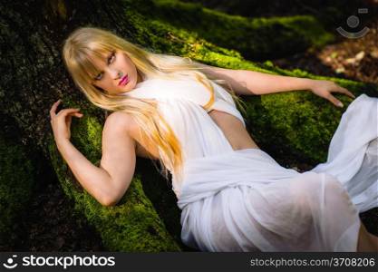 Beautiful woman wearing white garment and lean against the roots of old spruce, horizon format