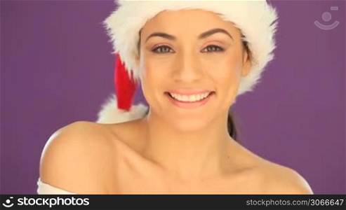 Beautiful woman with a beaming cheerful smile wearing a Santa hat against a purple studio background