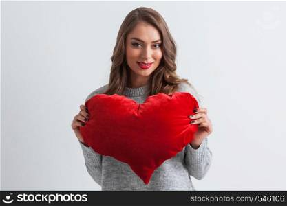 Beautiful woman with a big red heart shape pillow on white background. Woman with red heart pillow