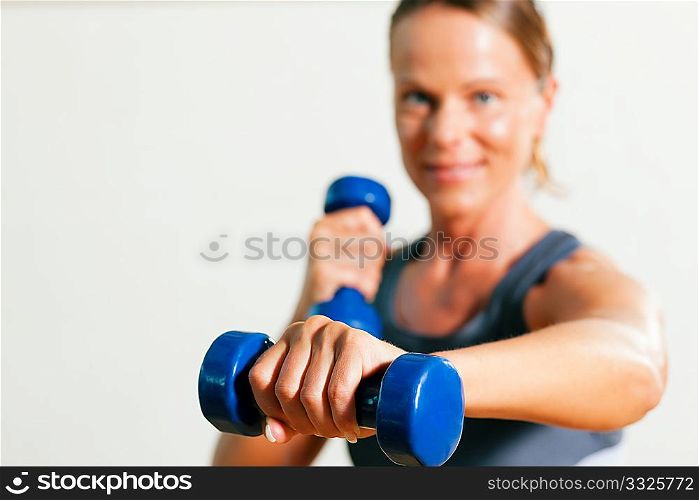 Beautiful woman with a dumbbell exercising in gym (focus is on the dumbbell!)