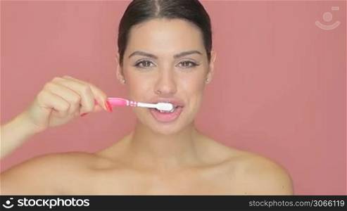 Beautiful woman with a lovely big smile holding a toothbrush and toothpaste in her hand on a pink studio background