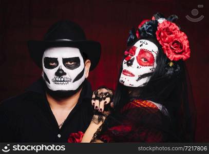 beautiful woman with a sugar skull makeup with a wreath of flowers on her head and a skeleton man in a black hat