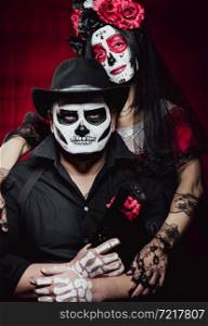 beautiful woman with a sugar skull makeup with a wreath of flowers on her head and a skeleton man in a black hat holding a gun