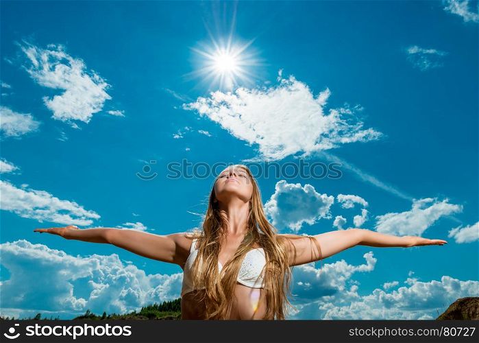 beautiful woman with arms outstretched against the background of the sun and sky in a bikini