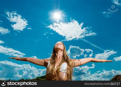 beautiful woman with arms outstretched against the background of the sun and sky in a bikini