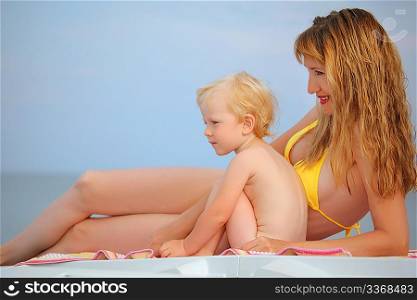 beautiful woman with blond little baby girl lying on beach, looking afar