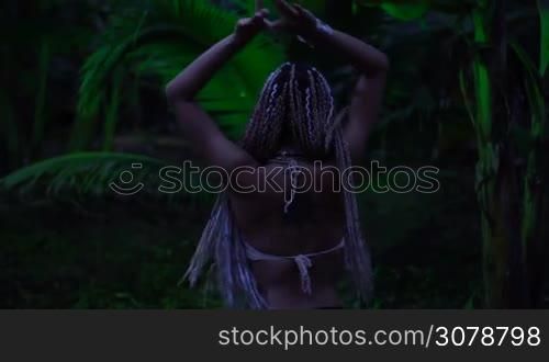 Beautiful woman with braids dancing near the palm tree in the jungle - video in slow motion
