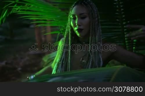 Beautiful woman with braids dancing near the palm tree in the jungle