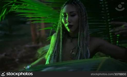 Beautiful woman with braids dancing near the palm tree in the jungle