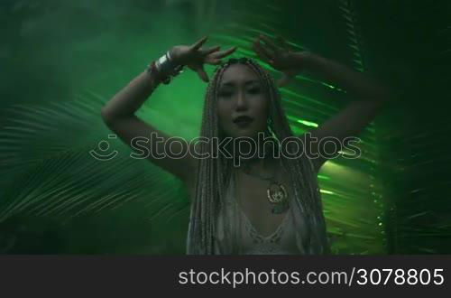 Beautiful woman with braids dancing near the palm tree in the jungle