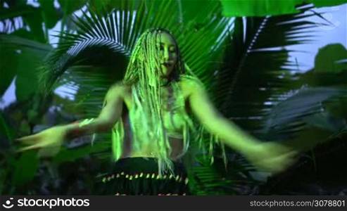 Beautiful woman with braids dancing near the palm tree in the jungle - low angle video