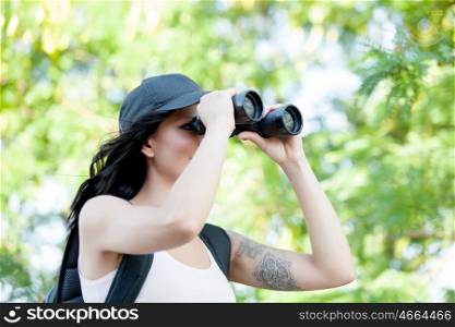 Beautiful woman with cap and backpack looking through binoculars while hiking trip