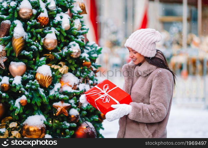 Beautiful woman with Christmas gift in the snow outdoors on a wonderful winter day. Happy girl near fir-tree branch in snow for new year.