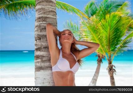 Beautiful woman with closed eyes standing near palm tree, enjoying amazing summer vacation on paradise beach 