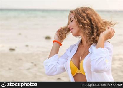 Beautiful woman with curly hair in bikini and white shirt enjoy summer vacation at tropical beach. Woman enjoy vacation on beach